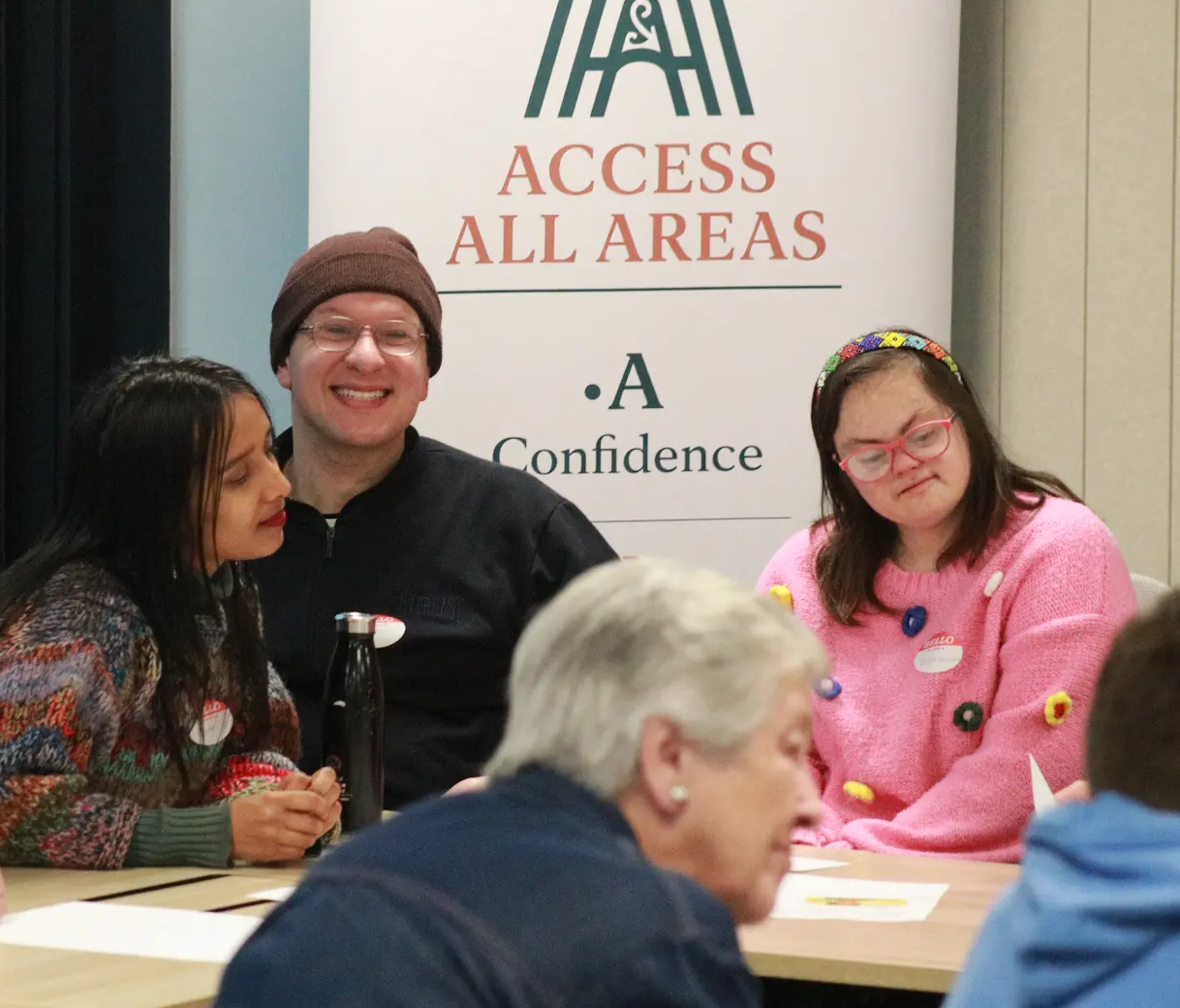 Sean Prenter sitting and smiling alongside two Access Lab participants in front of the Access All Areas banner