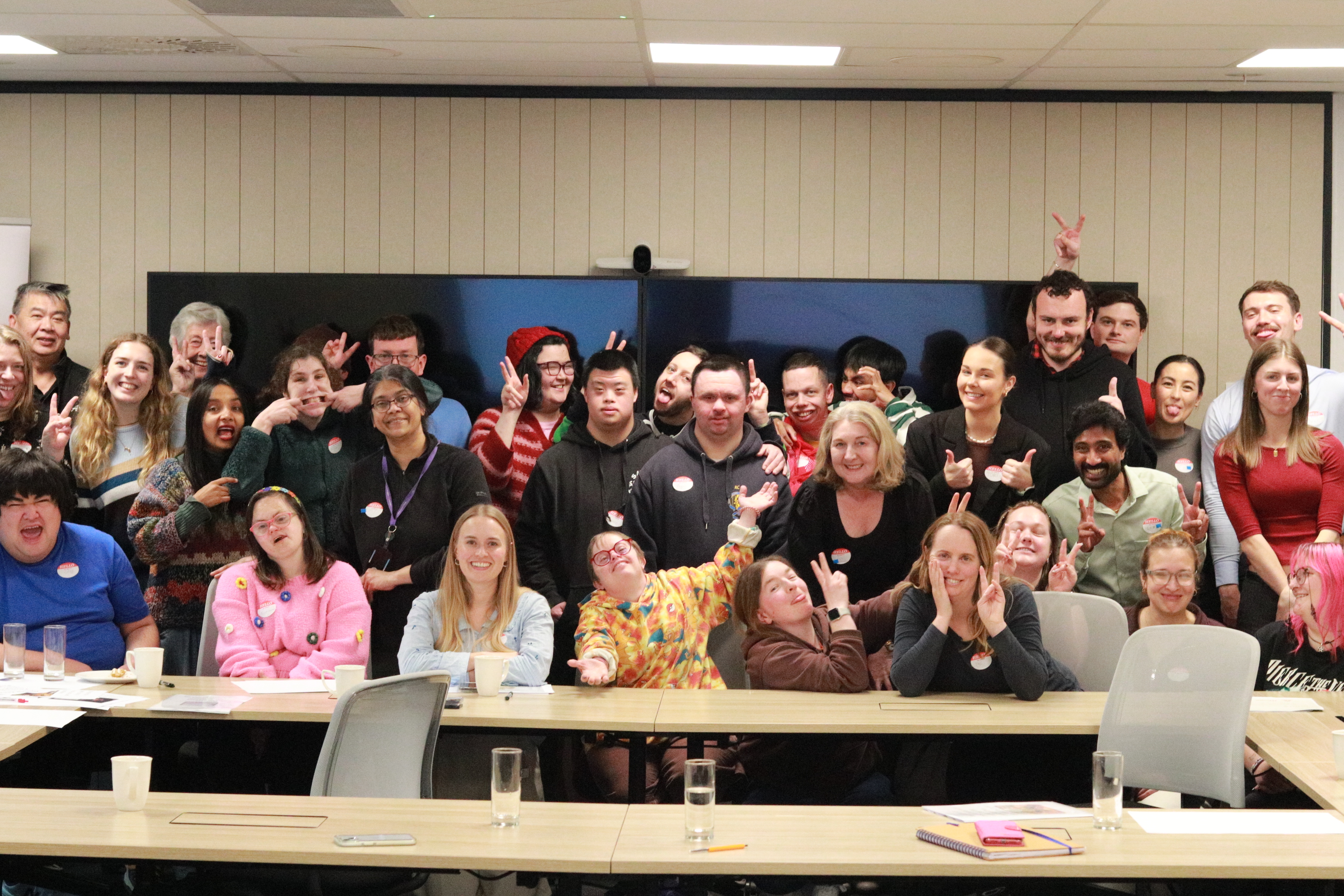 A large group of Access Lab participants, volunteers, and mentors smiling together around the boardroom table
